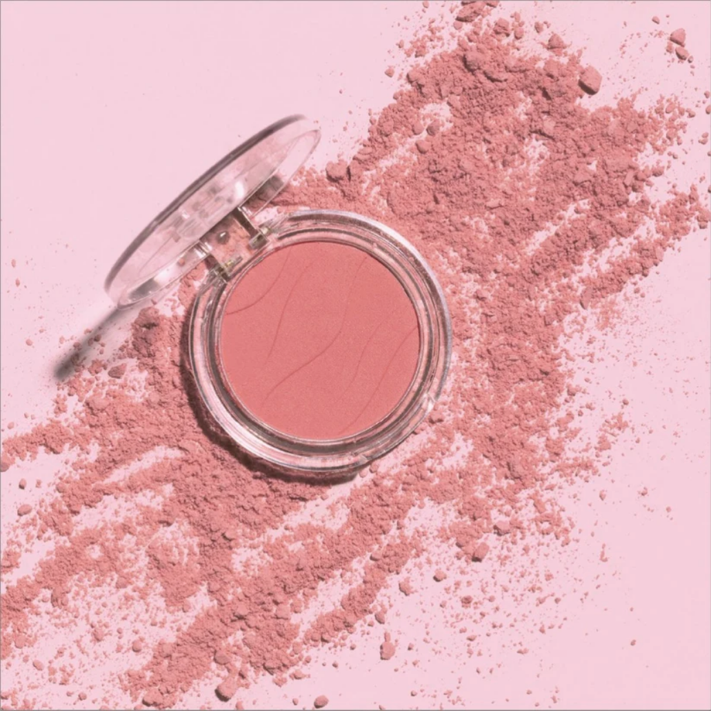 Soft Glow Blusher in een transparante verpakking, met een zachte roze kleur en poederachtige textuur op een roze achtergrond.