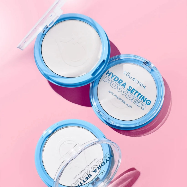 Hydra Setting Powder - Transparant in een ronde, doorzichtige verpakking met blauwe accenten, op een roze achtergrond.